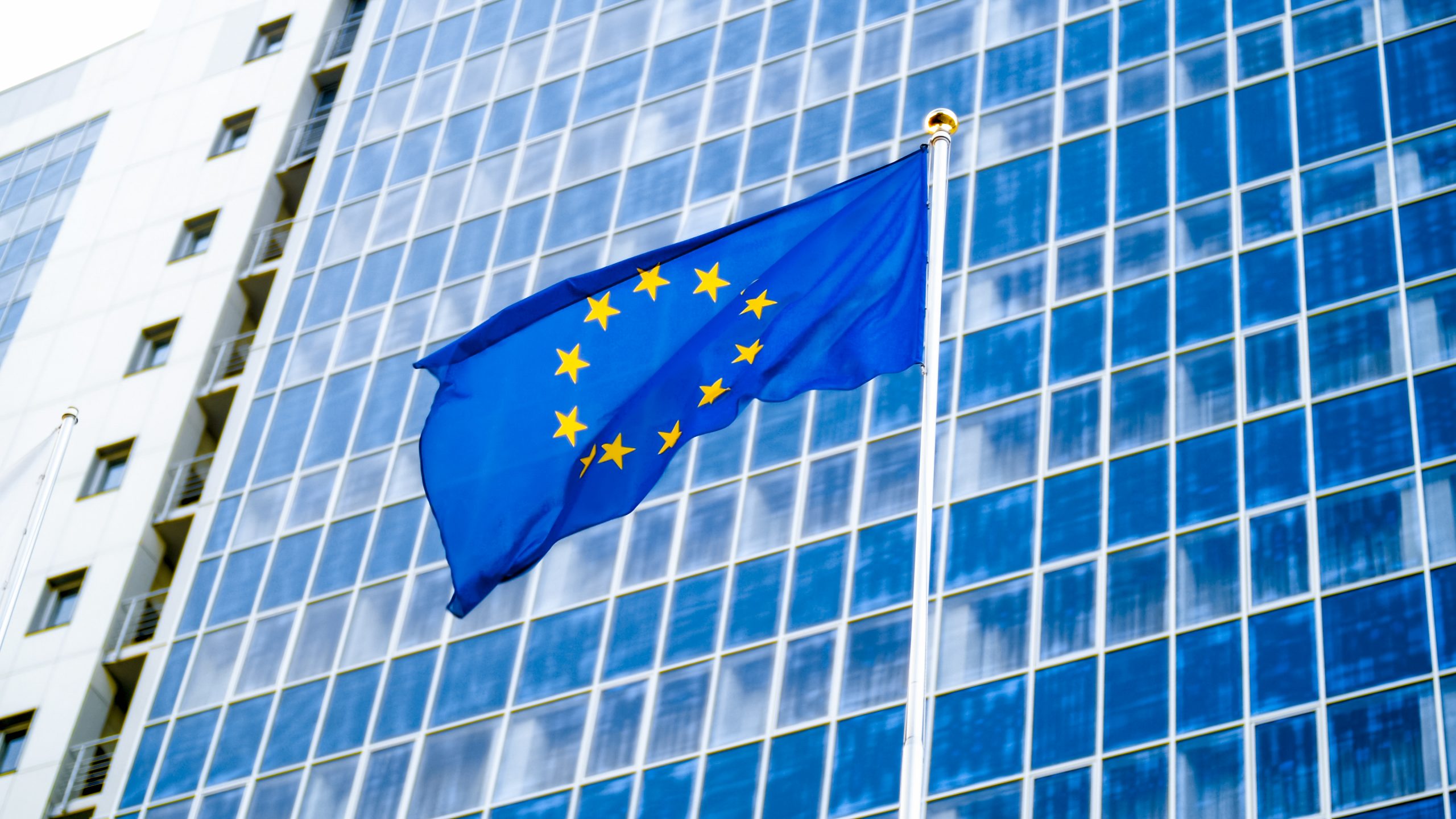 image of eu flag fluttering on wind against high business office building made of concerete and glass. concept of ecenomics, development, government and politics
